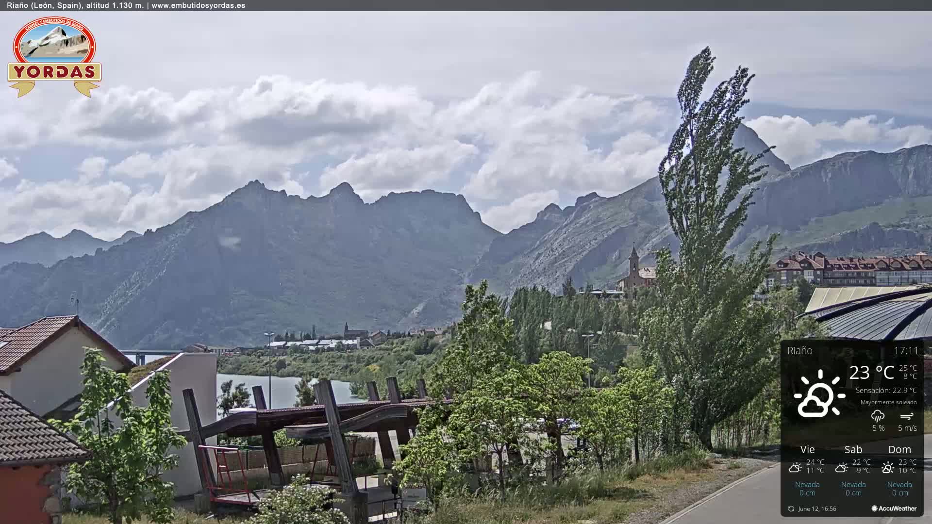 A partly cloudy day reveals a mountainous landscape with a town nestled beside a river,  and a playground partially visible in the foreground.