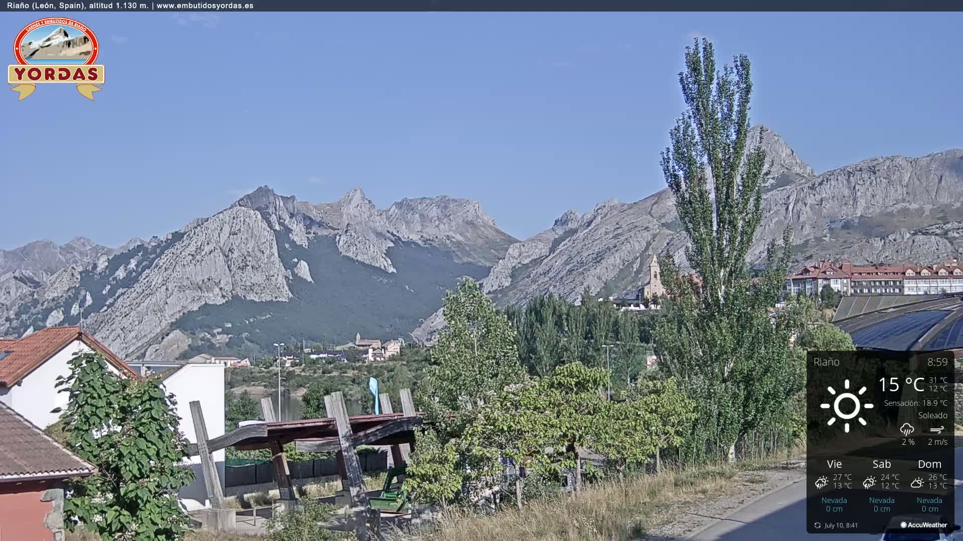 A sunny view of a town nestled in a valley, with imposing mountains in the background.