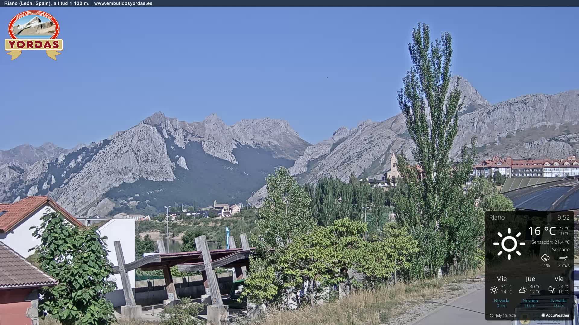 A sunny view of a town nestled in a valley, surrounded by large, light-grey mountains.