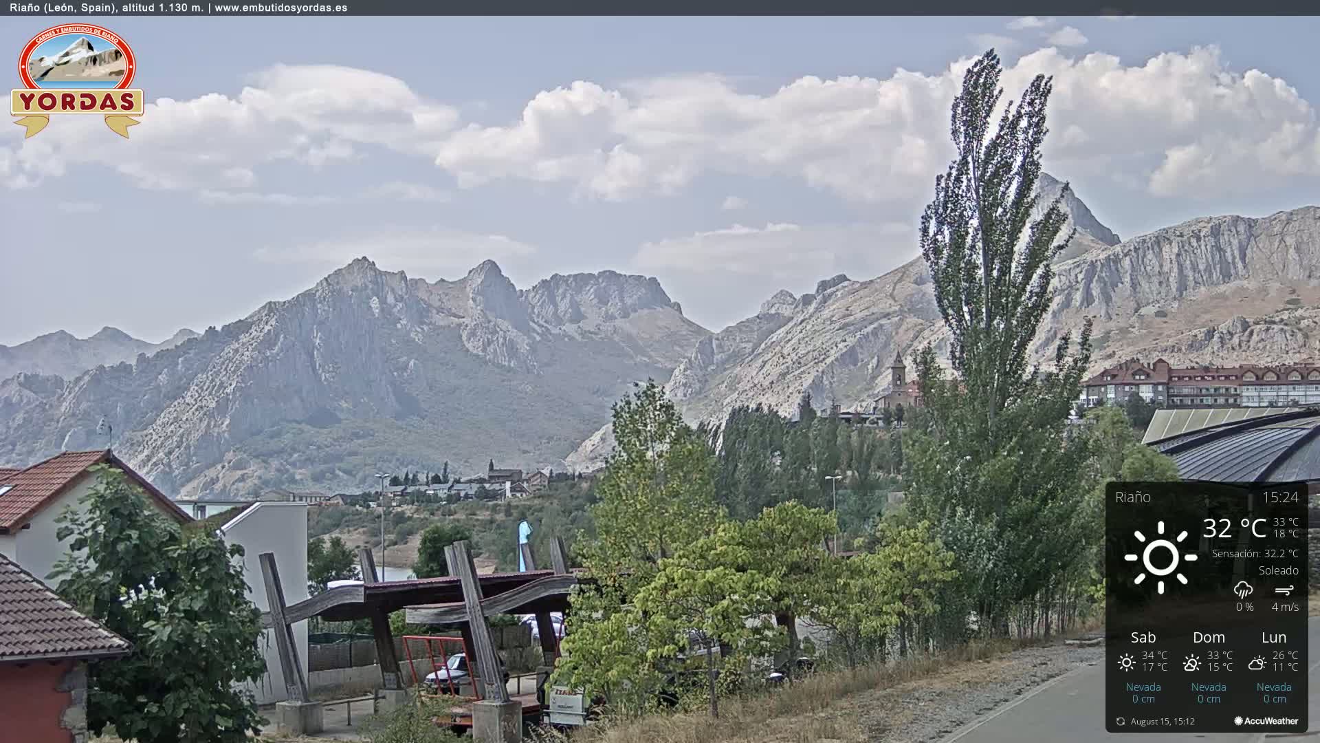 A sunny view of a town nestled in a valley, with large, light-grey mountains in the background.