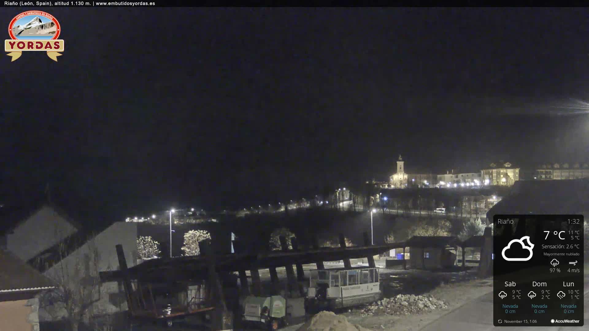 The image depicts a nighttime landscape of a town with numerous illuminated buildings and streetlights, along with foreground structures that appear to be part of a construction site, under mostly cloudy skies.