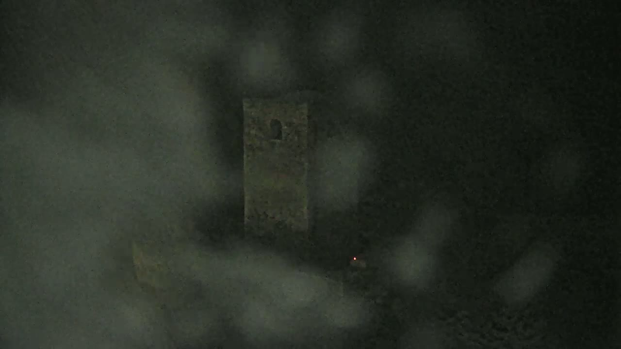 A stone tower is barely visible through a thick fog at night.