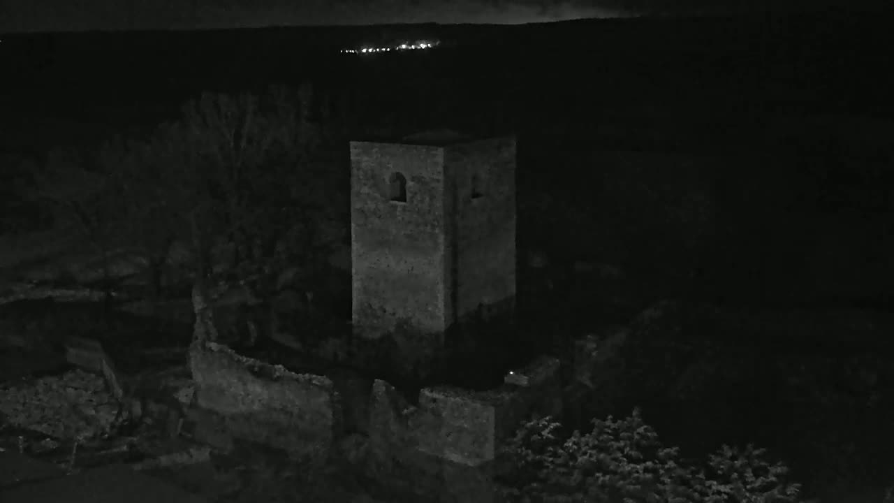 A stone tower, part of a ruined structure, stands in the dark of night under a cloudy sky.
