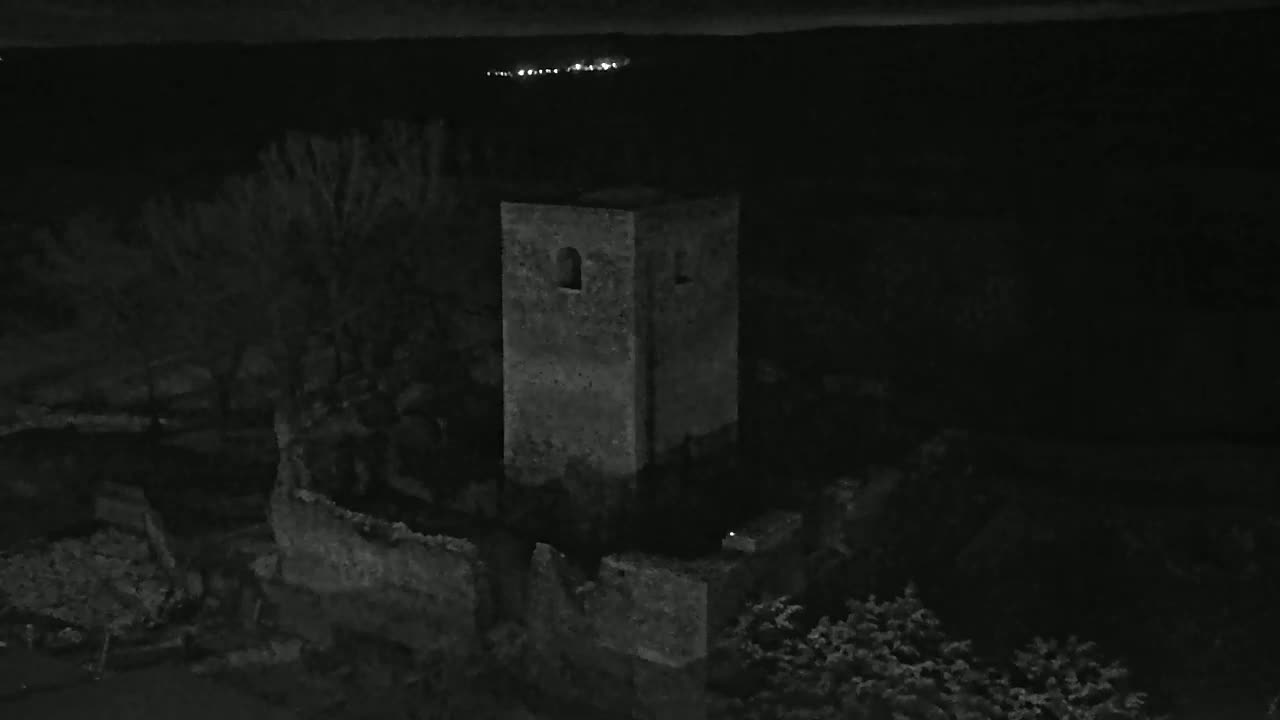 A stone tower and surrounding ruins are visible at night, under a dark sky with distant lights.