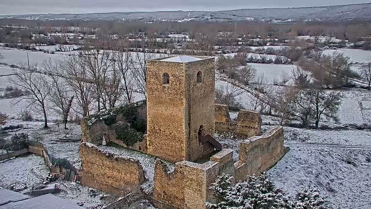 A stone tower and ruined walls of a building stand in a snow-covered landscape under an overcast sky.
