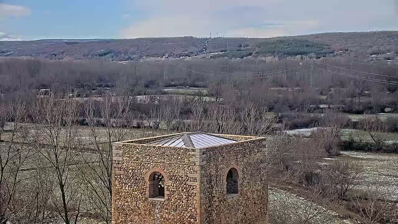 A stone tower with a flat roof stands in a snow-dusted landscape of leafless trees and fields under a mostly clear sky.