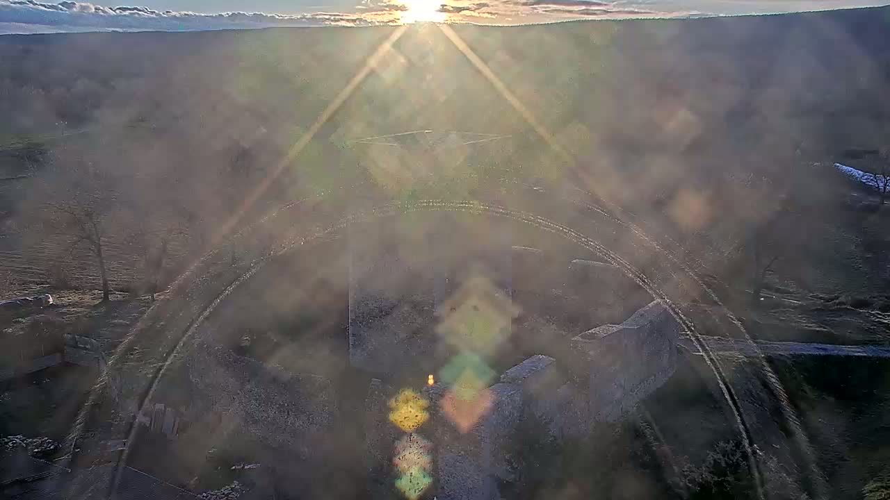 An aerial view shows the ruins of a stone structure on a hazy, sun-drenched landscape.