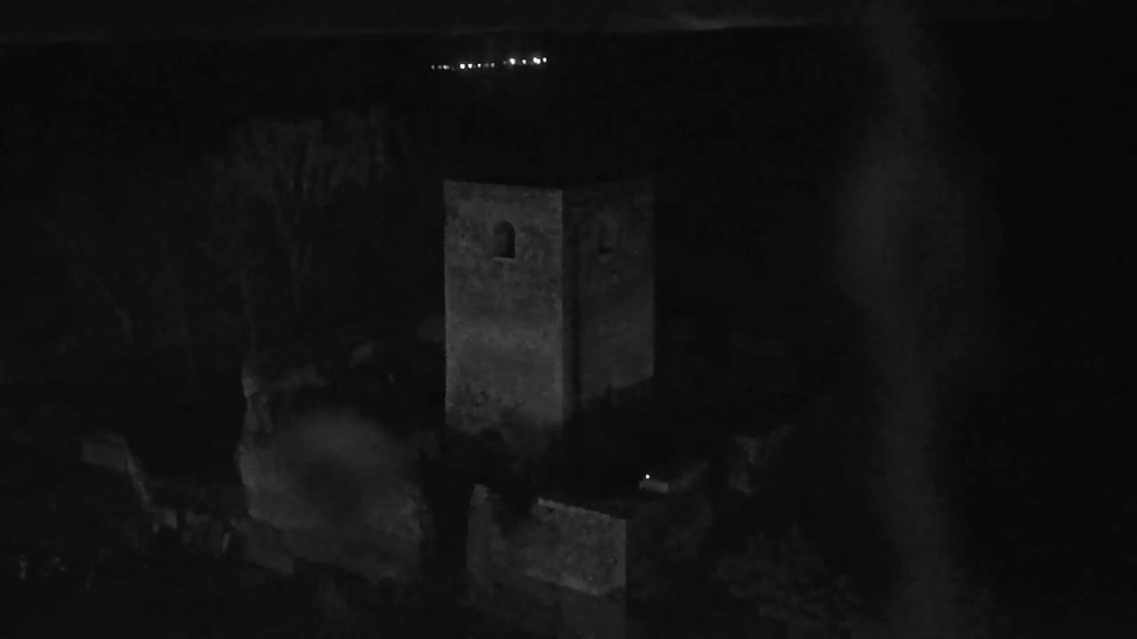 A dark gray stone tower stands in the darkness of night, illuminated faintly by distant lights.