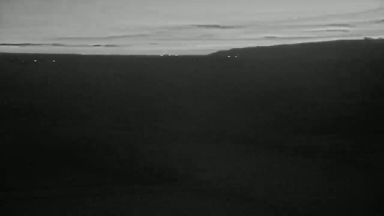 A dark, flat landscape extends to a distant, faintly lit horizon under a dusky sky.
