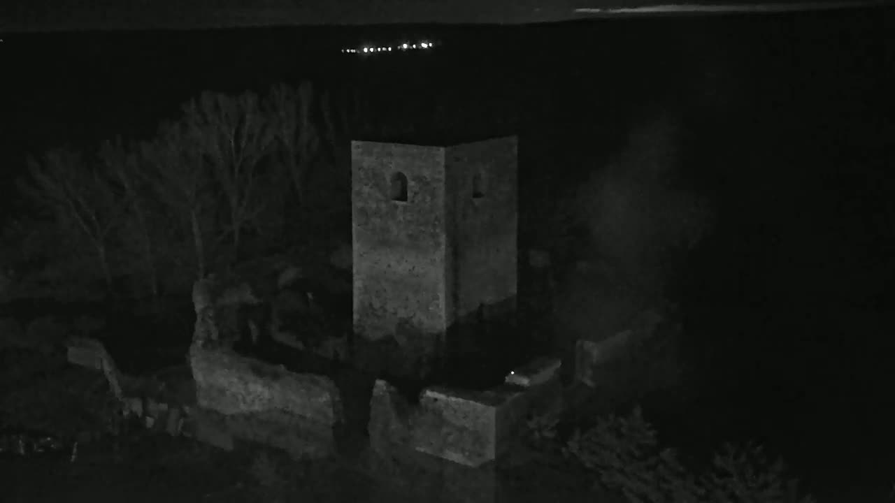 A stone tower and surrounding ruins are visible at night, under a dark sky with distant lights.