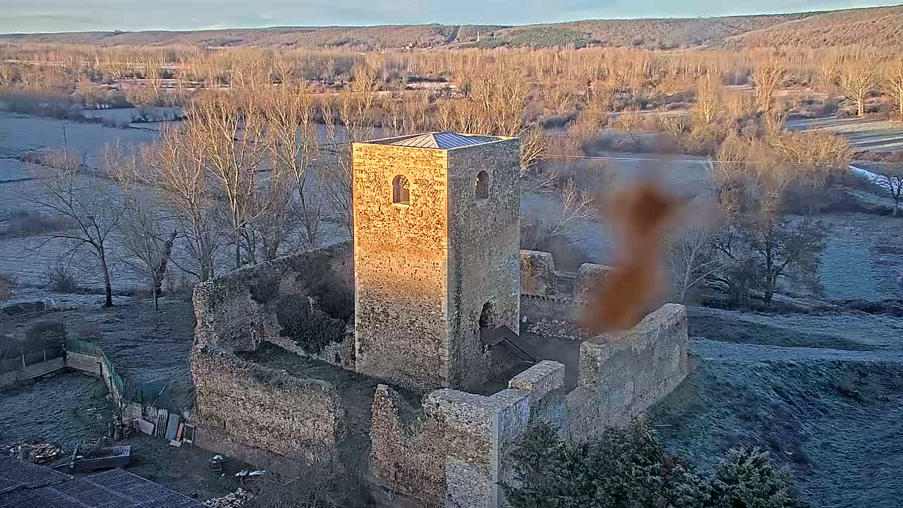 A stone tower and the ruins of a larger structure are situated in a frost-covered landscape under a clear, bright sky.