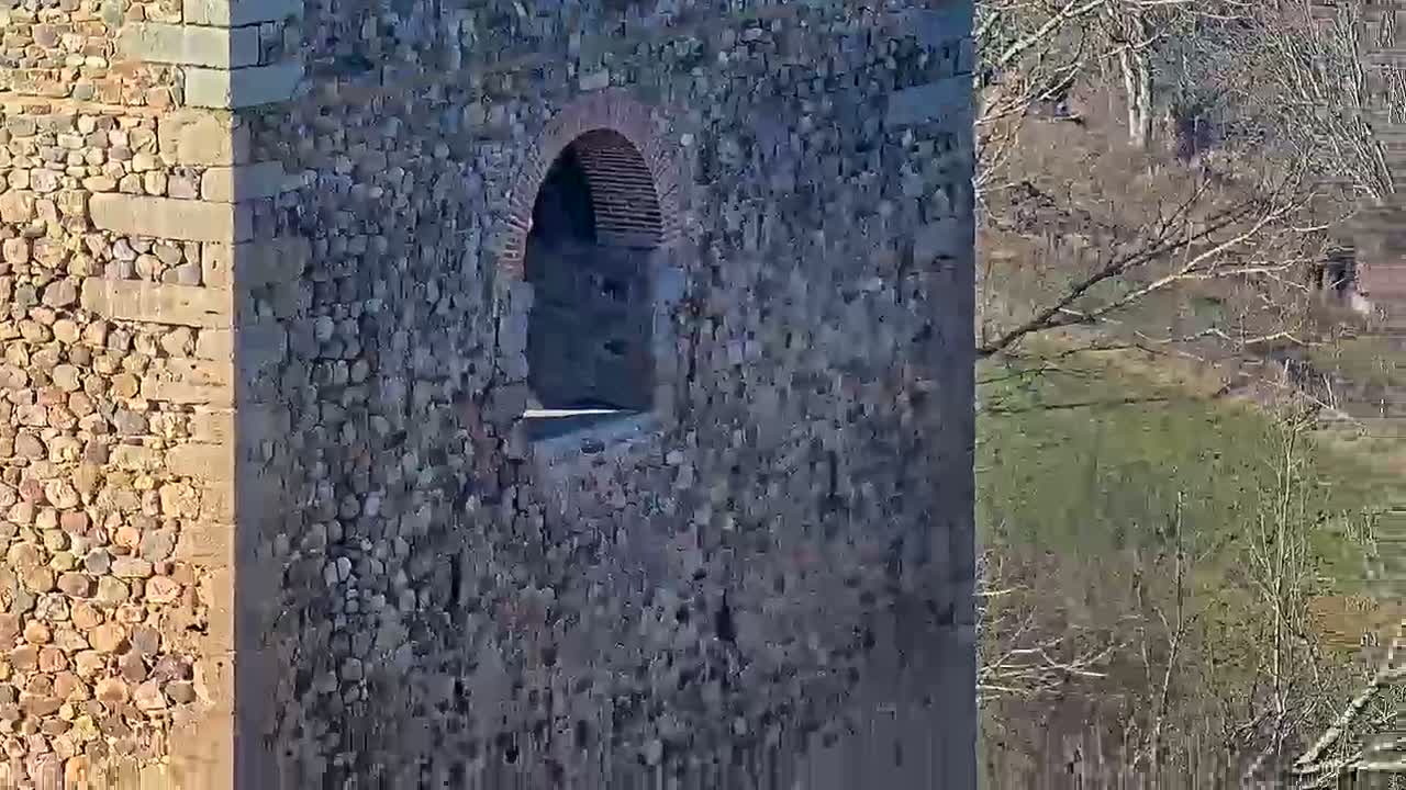 A stone tower with a small arched opening is seen, partially shadowed, overlooking a bare, wintry landscape.