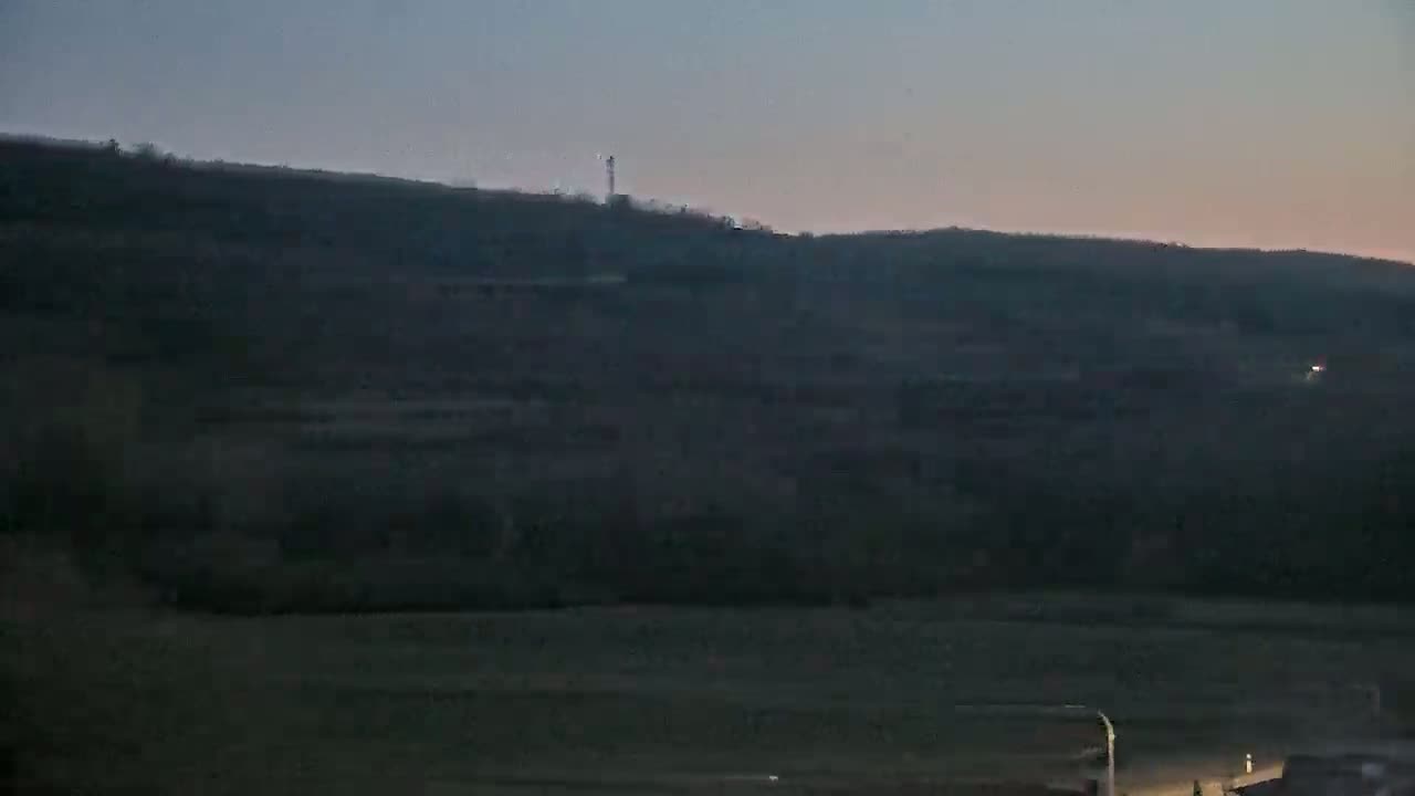 A dark, hilly landscape is visible at dusk or dawn under a clear, dusky sky.