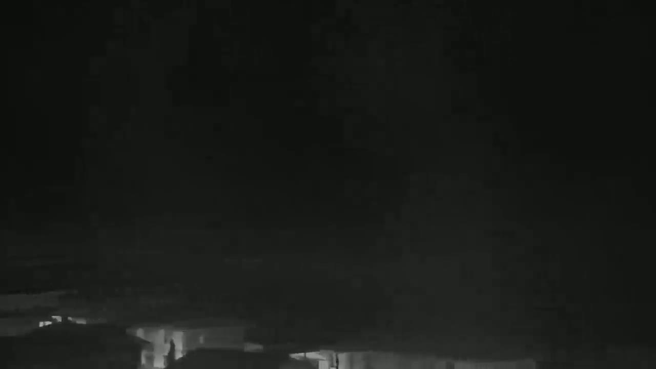 A low-light nighttime image shows the tops of buildings under a dark, cloudy sky.