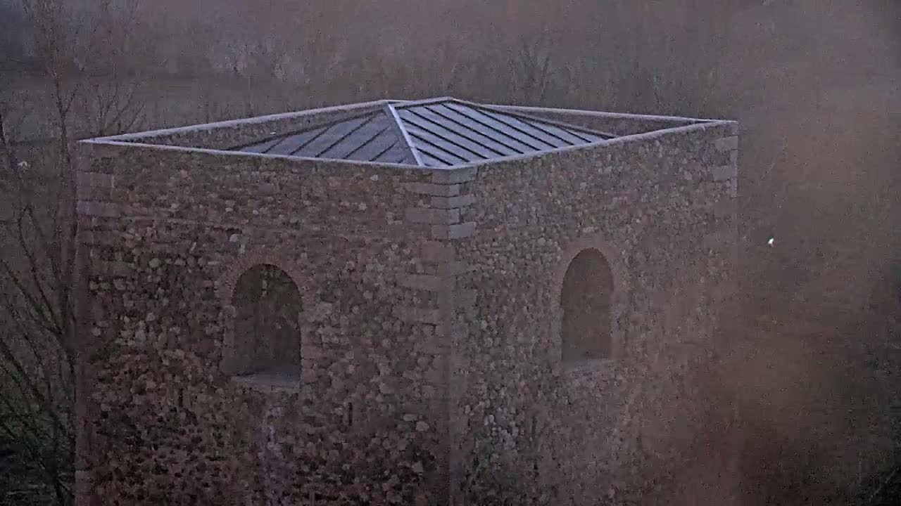 A stone structure with a metal roof and arched openings is seen in hazy outdoor conditions.