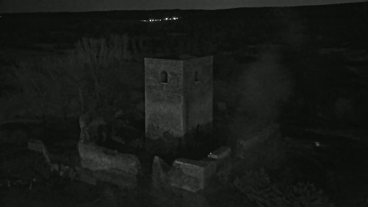 A stone tower, partially ruined, stands under a dark night sky.