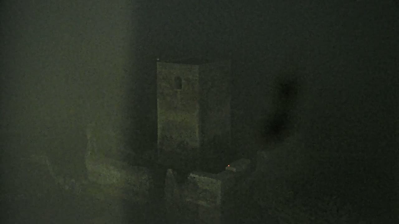A dark, foggy view shows a stone tower and surrounding structures at night.