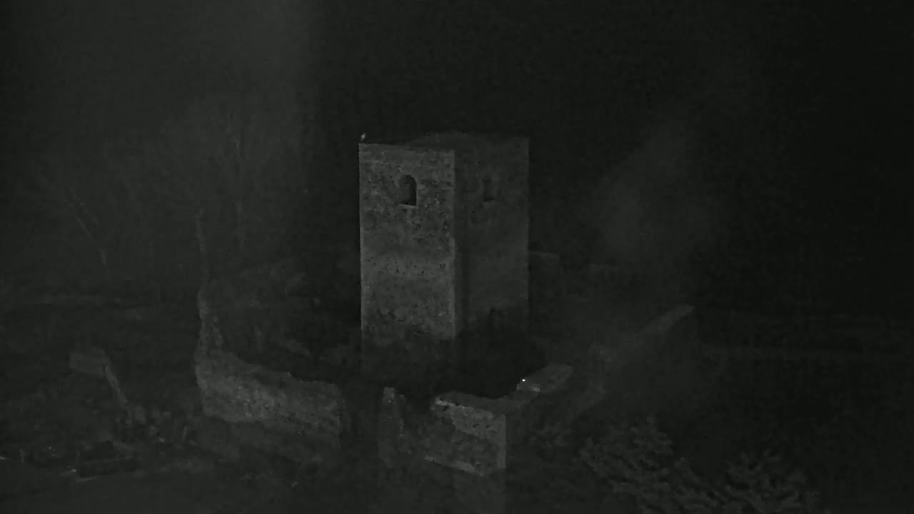 A stone tower and surrounding ruins are shrouded in mist or fog at night.