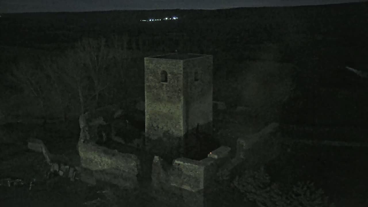 An aerial nighttime view shows the ruins of a stone tower and surrounding walls under a dark sky.