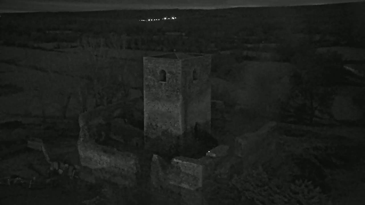 At night, the ruins of a stone tower and surrounding walls are visible, set against a dark, rural landscape.