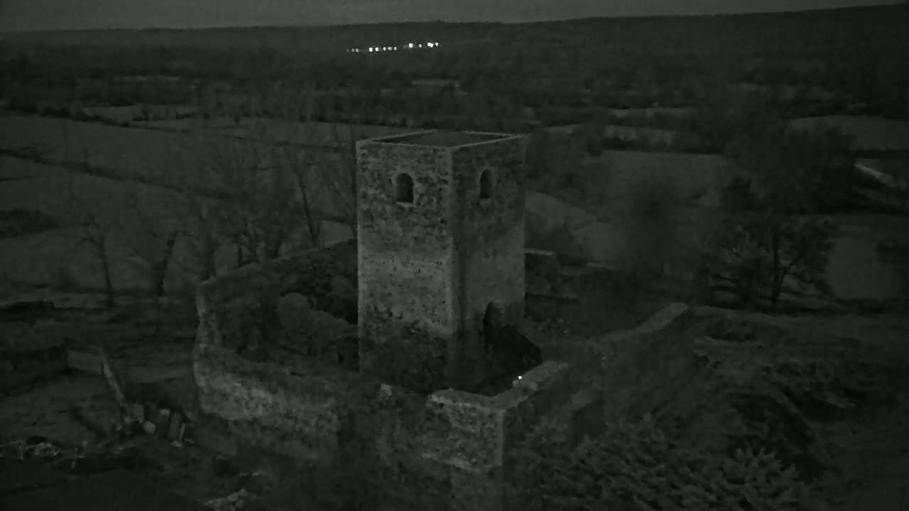 An aerial, nighttime view shows the stone ruins of a tower and surrounding buildings in a dark, rural landscape.