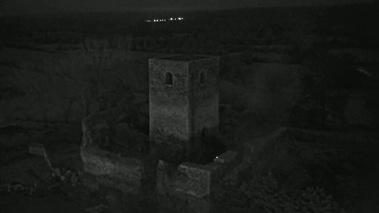 A stone tower, part of a larger ruin, is visible at night under a dark sky with distant lights.