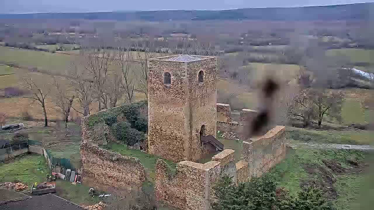 An aerial view shows the stone ruins of a tower and surrounding walls on a cloudy day in a rural landscape of bare trees and fields.