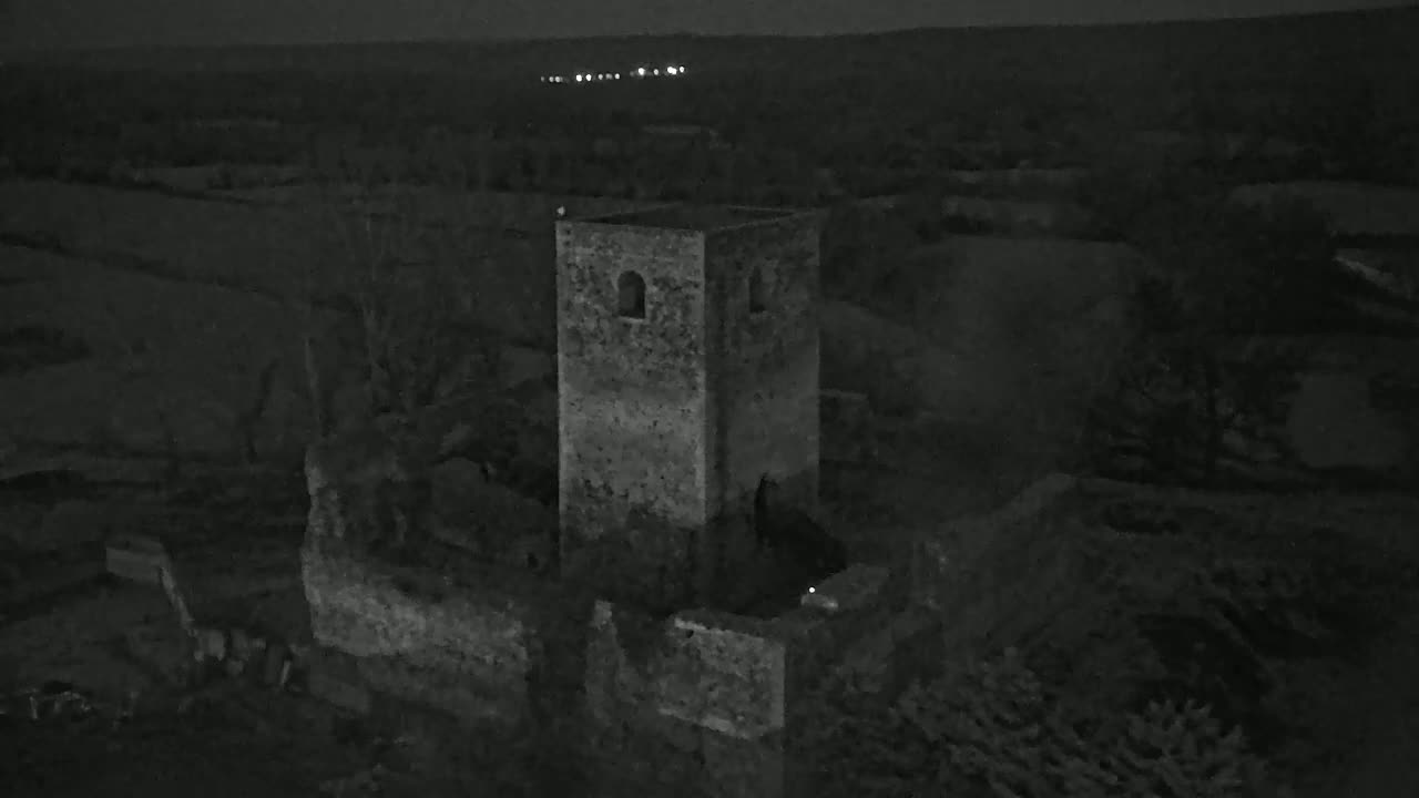 A stone tower ruin stands at night in a dark, rural landscape under a clear sky.