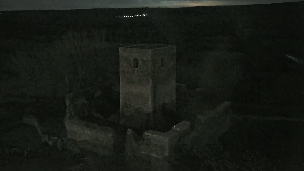 An old, stone tower, part of a larger ruin, is visible at night under a dark sky.