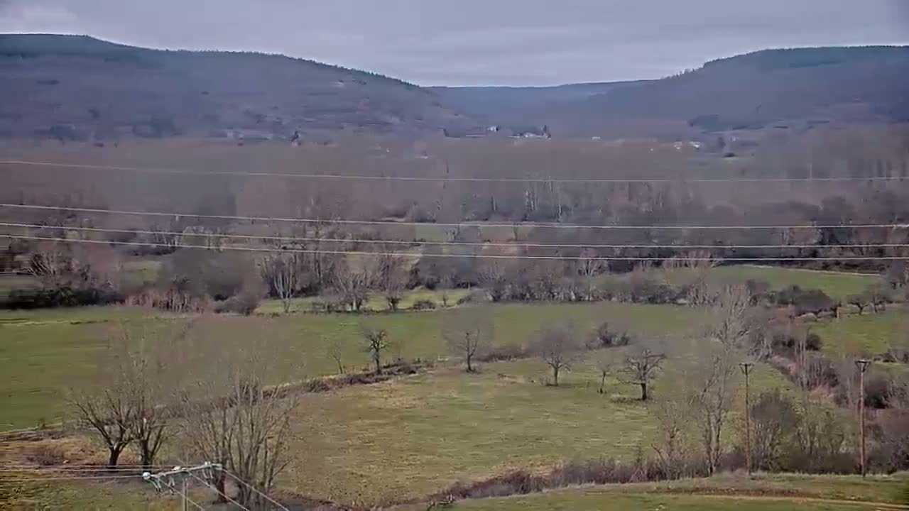 A view of a valley under an overcast sky shows barren trees and fields stretching to distant hills.