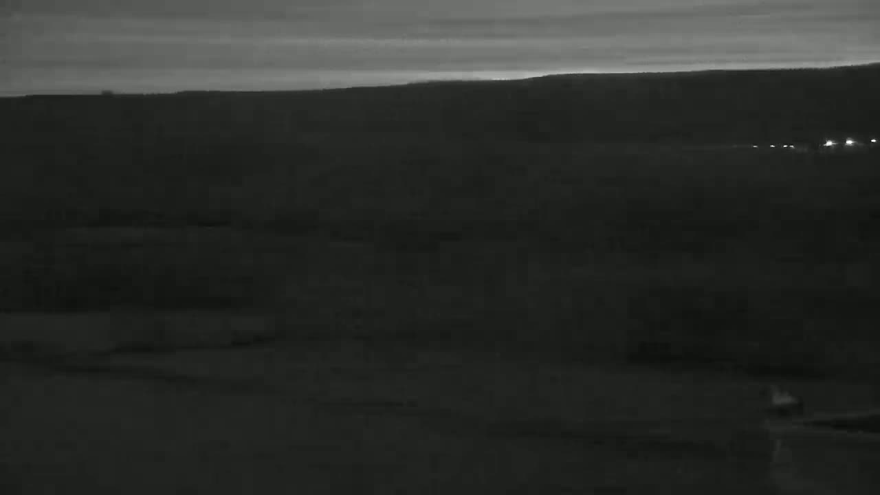 A dark, flat landscape is visible under a dusky sky, with a few distant lights indicating a road.