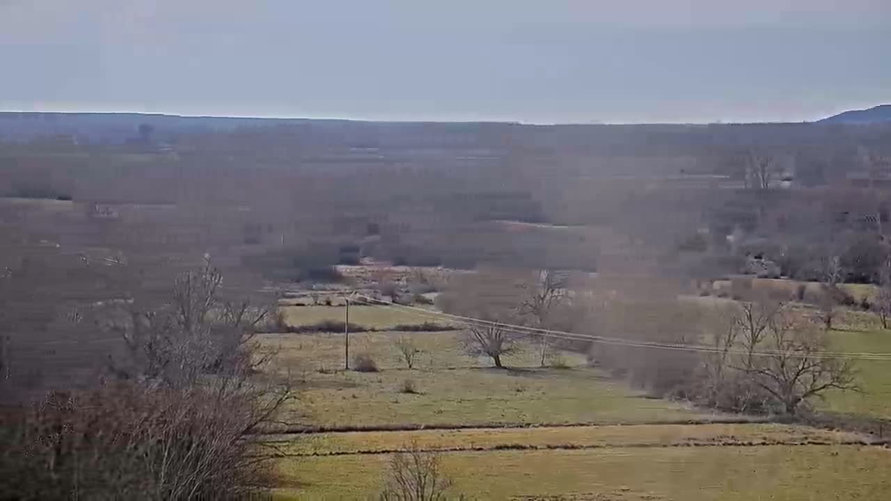 A hazy, distant view of a rural landscape with bare trees and fields under a light overcast sky.