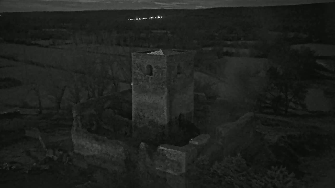 An aerial nighttime view shows the stone ruins of a tower and surrounding landscape under a dark sky.