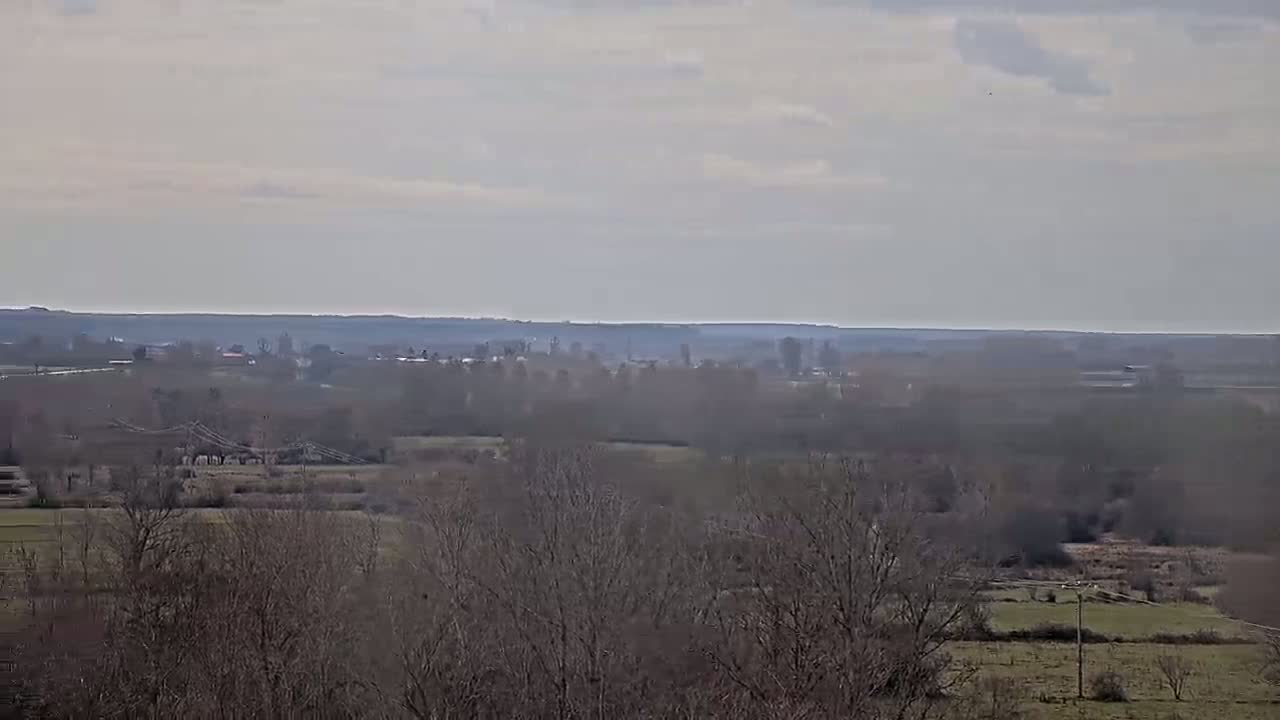 A hazy, overcast day reveals a vast, flat landscape of leafless trees, fields, and distant settlements.