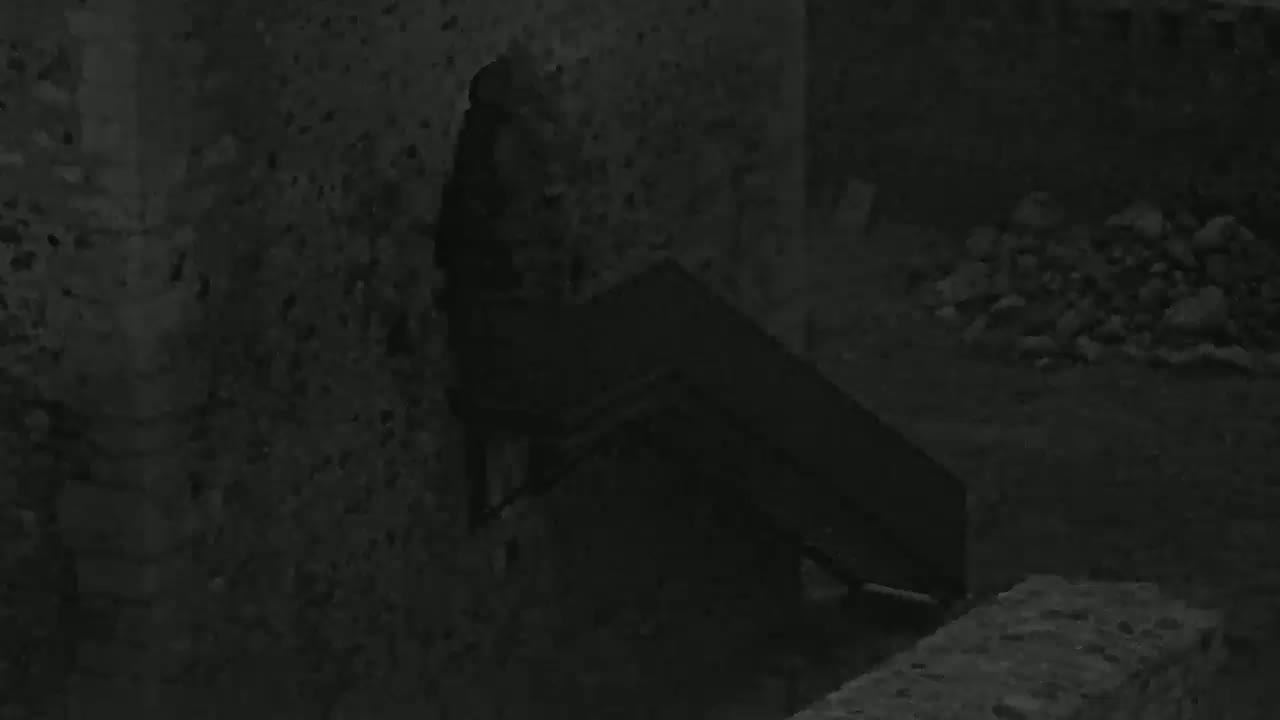 A dark, possibly nighttime, scene shows a stone wall with a dark, seemingly wooden, staircase attached.