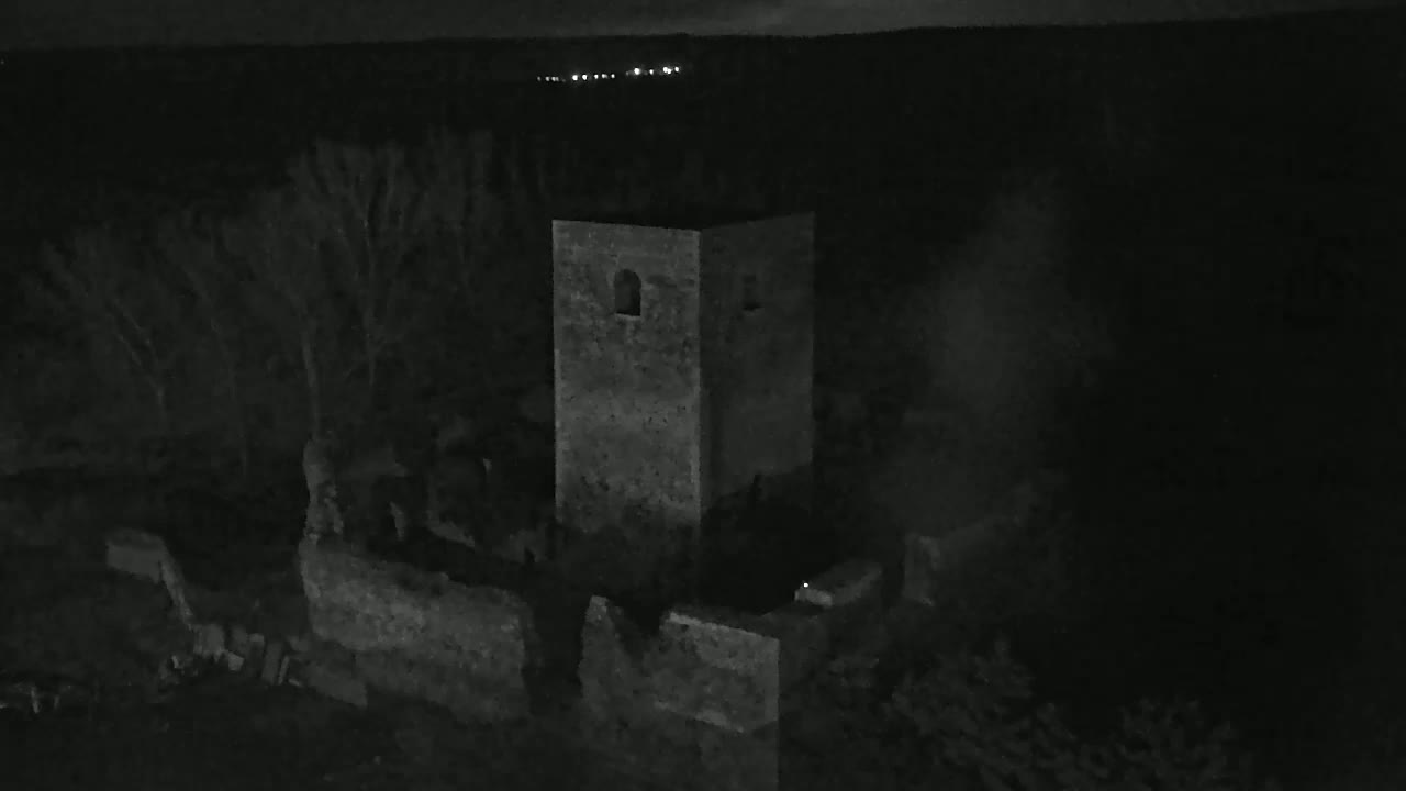 A stone tower and surrounding low walls are visible at night, under a dark sky with distant lights.