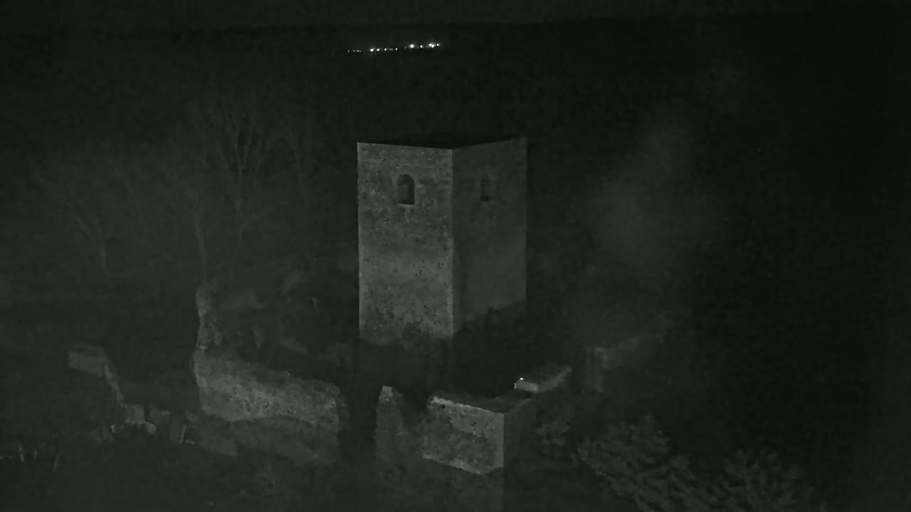 A stone tower and surrounding ruins are visible at night, under hazy or foggy conditions.