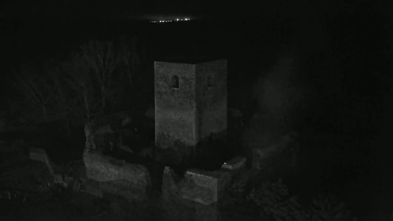 At night, a stone tower and surrounding ruins are dimly visible, with a faint light source in the distance.