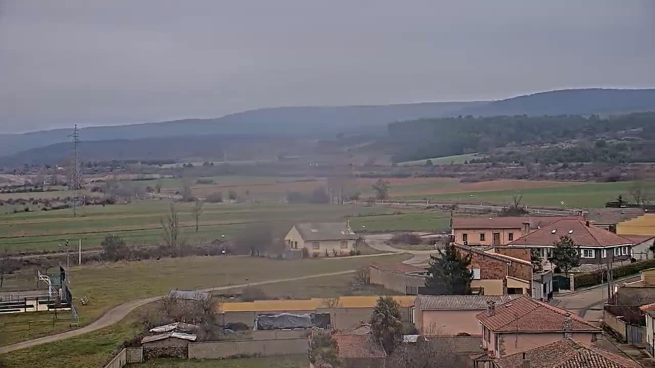 A hazy, overcast day reveals a sprawling rural landscape, featuring a small village nestled amongst fields and distant hills.