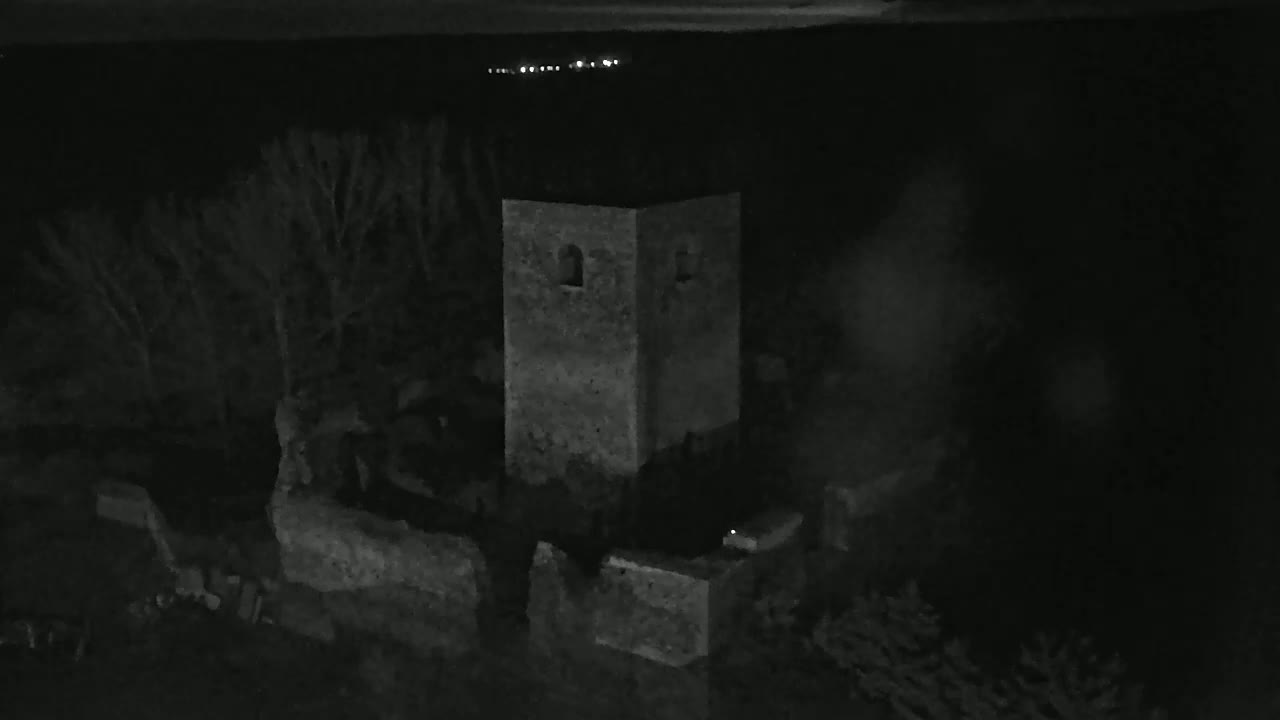 A stone tower and surrounding ruins are visible at night, under a dark sky with distant lights.