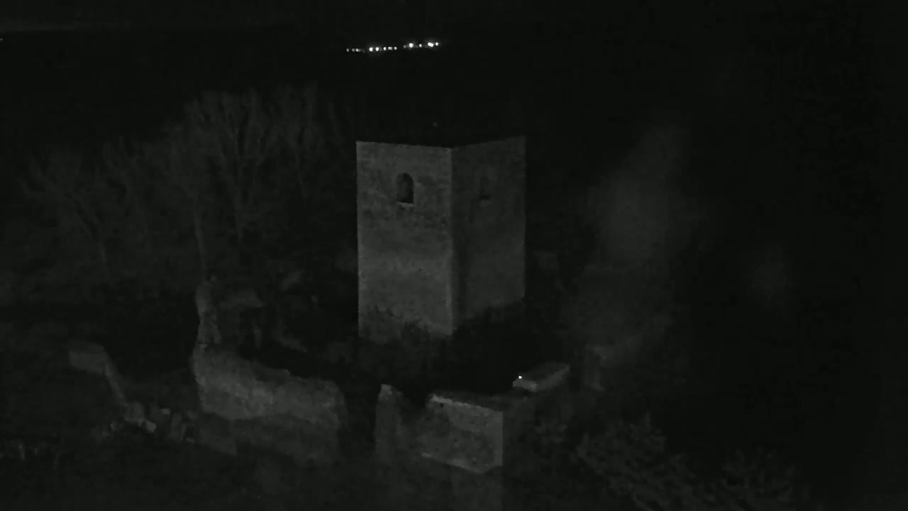 A stone tower and surrounding low walls are visible at night, with some trees and a faint fog or mist in the air.