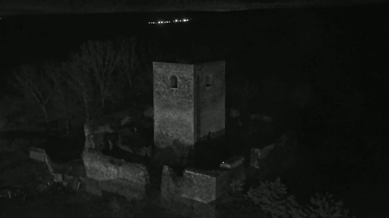 A stone tower and surrounding ruins are visible at night, under a dark sky with distant lights.
