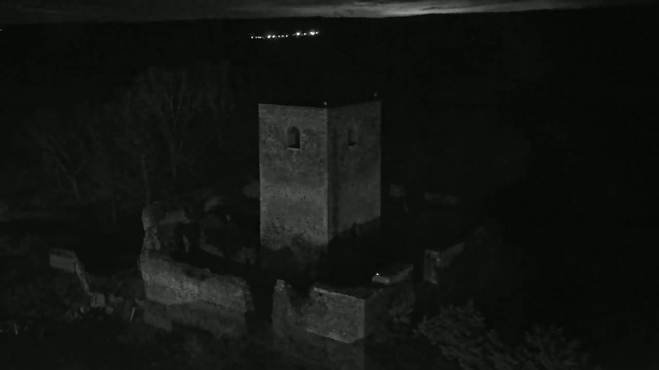 An aerial view at night shows the stone ruins of a tower and surrounding walls, under a dark sky.