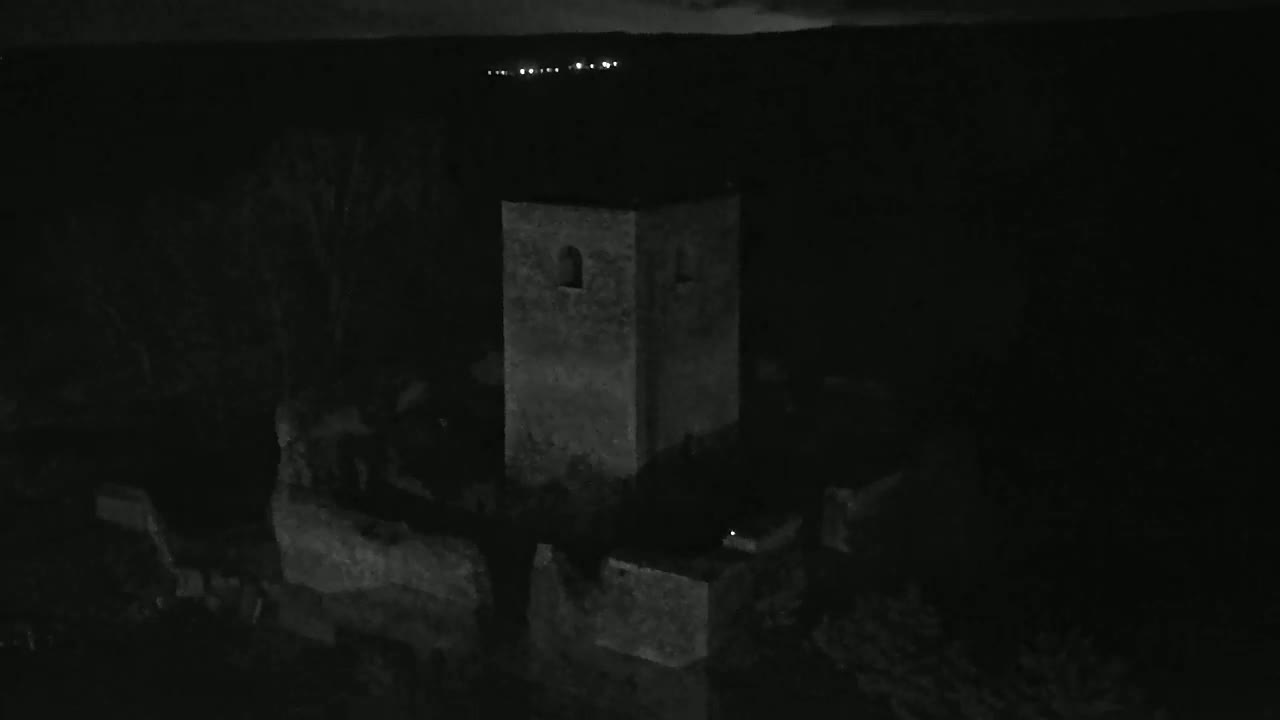 A stone tower, part of a larger stone structure, stands silhouetted against a dark, nighttime landscape.