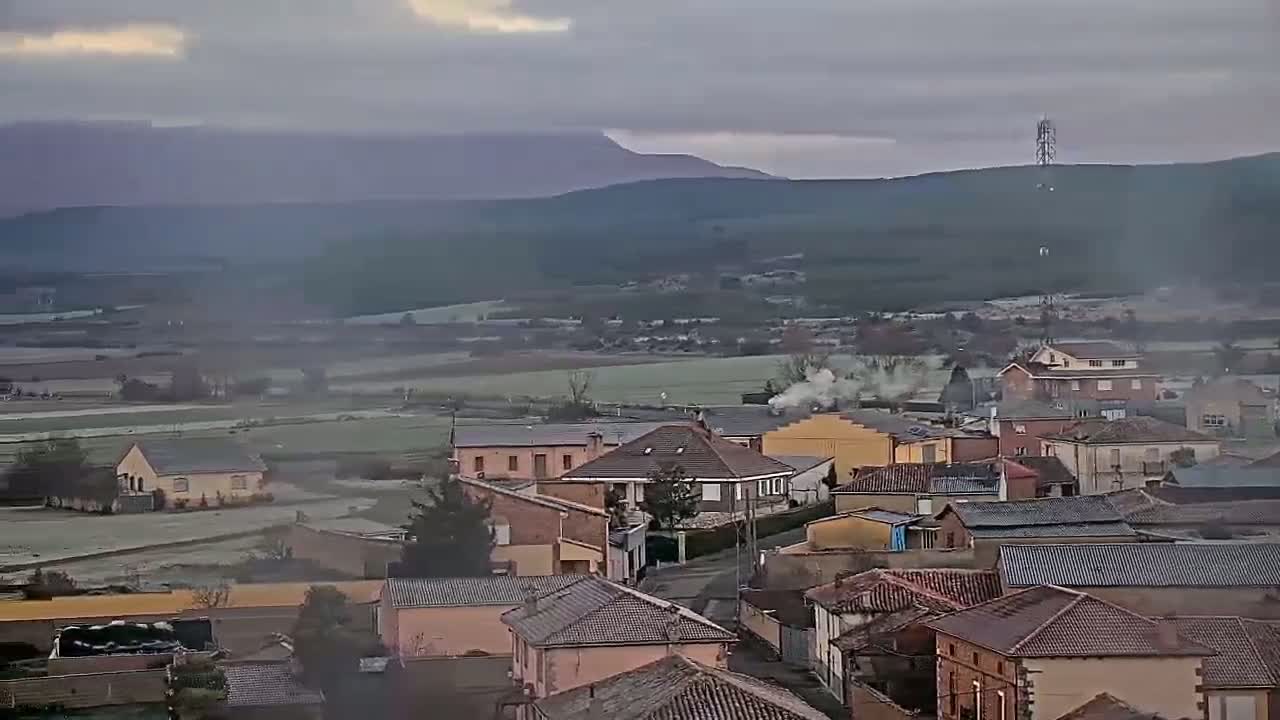 A hazy, overcast day reveals a small town nestled in a valley, with rolling hills and distant mountains in the background.
