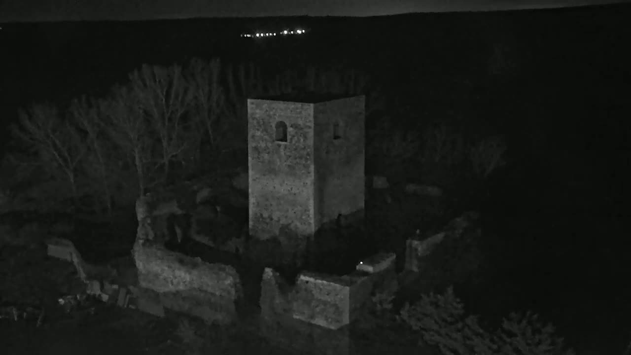 A stone tower and surrounding ruins are visible at night, under a dark sky with distant lights.