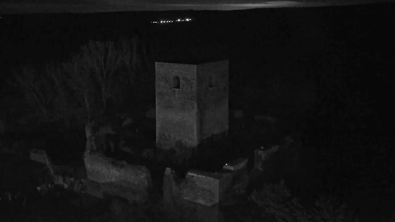A stone tower, part of a larger ruin, stands silhouetted against a dark, nighttime landscape.