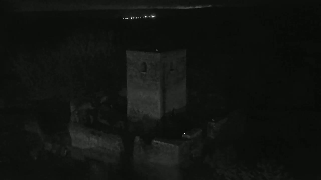 A stone tower is visible at night, with faint lights in the distance.