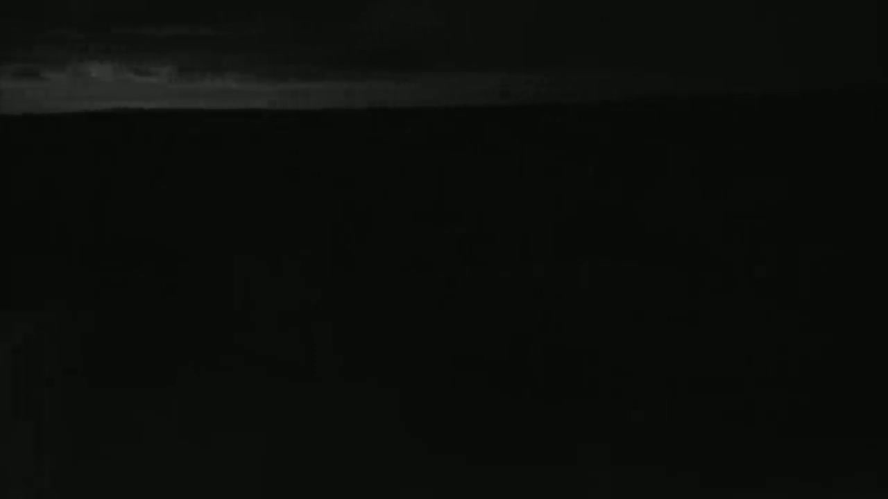 A dark, nighttime scene shows a mostly obscured landscape under a cloudy sky.