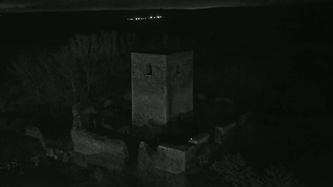 A stone tower, part of a larger ruin, stands silhouetted against a dark, night sky.